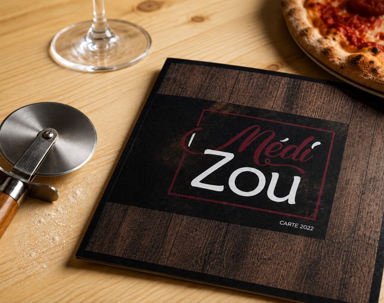 Création de menu pour MédiZou – Pizzeria artisanale en Seine-et-Marne Menu de la pizzeria MédiZou présenté sur table en bois avec pizza artisanale et roulette à pizza